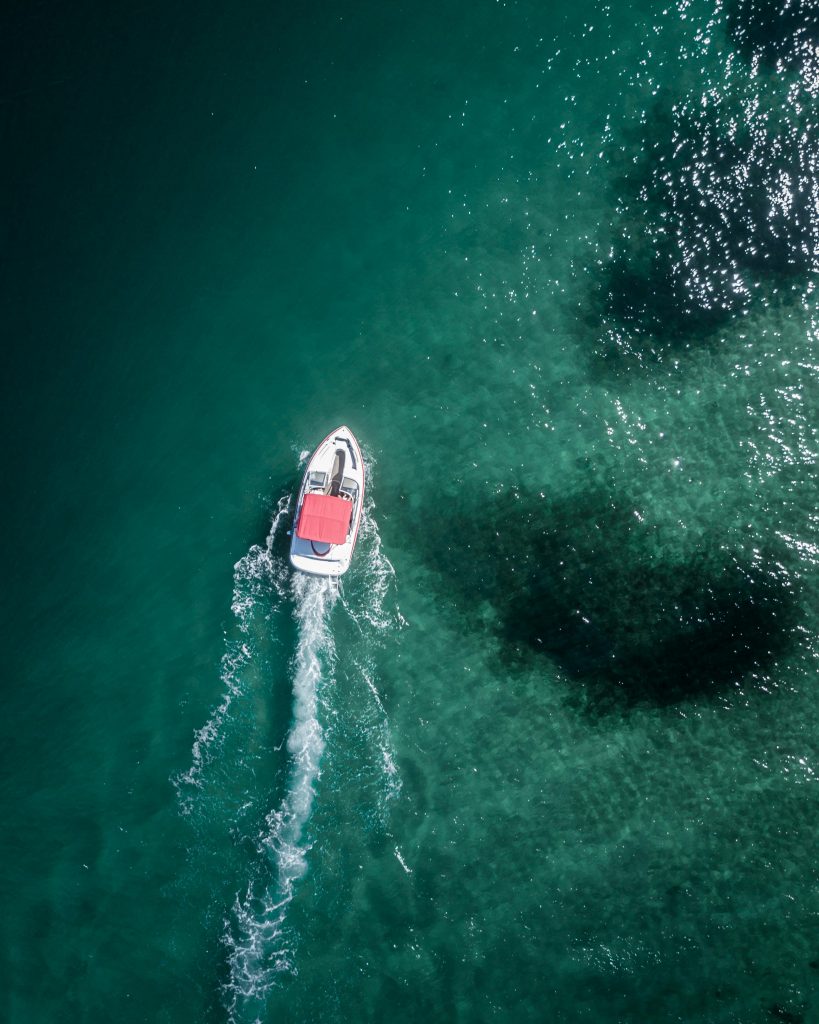 Aerial shot of a small boat with a red canopy cruising over Sydney's vibrant ocean waters, capturing the spirit of adventure.